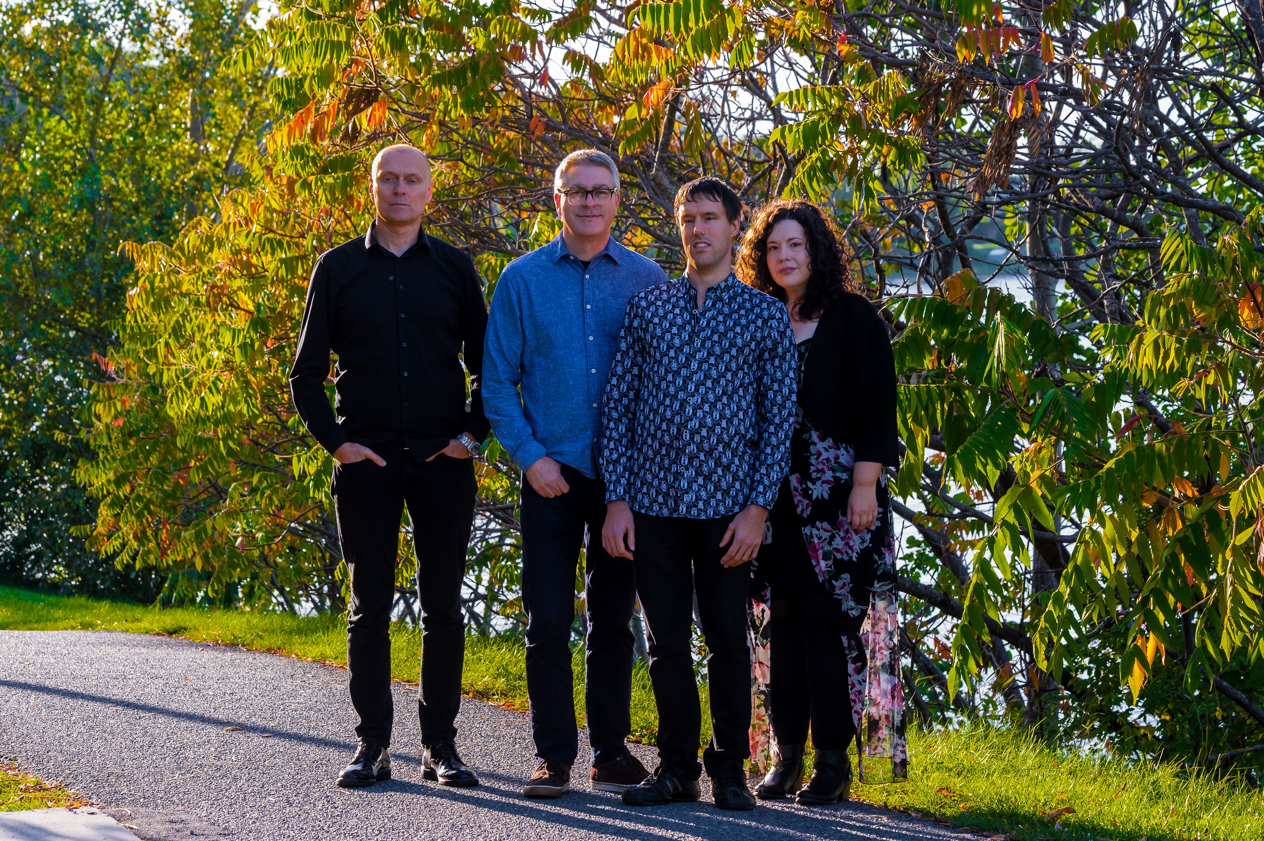 The Lucas Hanneman Express Blues Band in a group pose on a sunny summer's day on a roadside, in front of trees